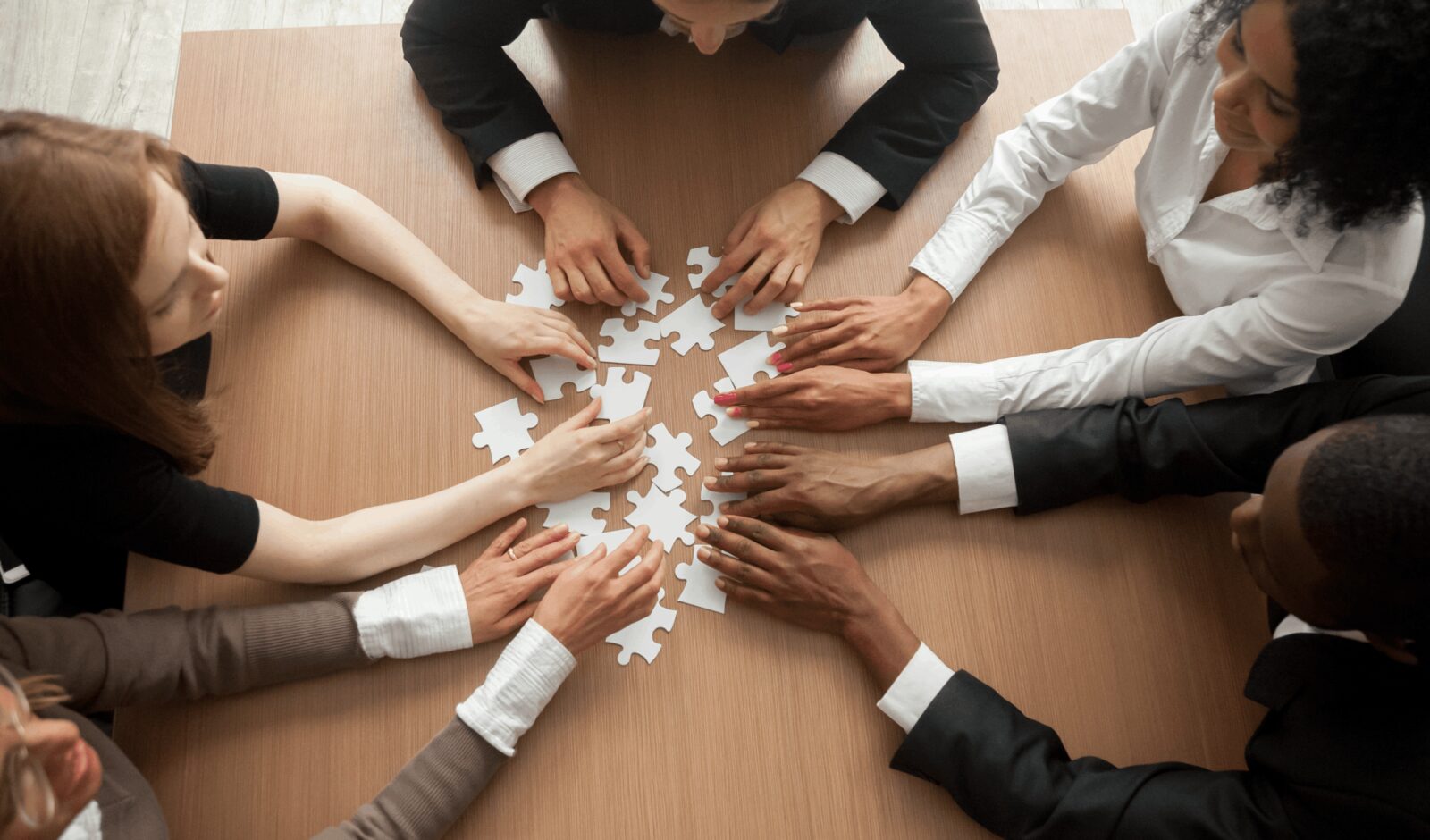 Team members fitting puzzle pieces together on a table, viewed from above