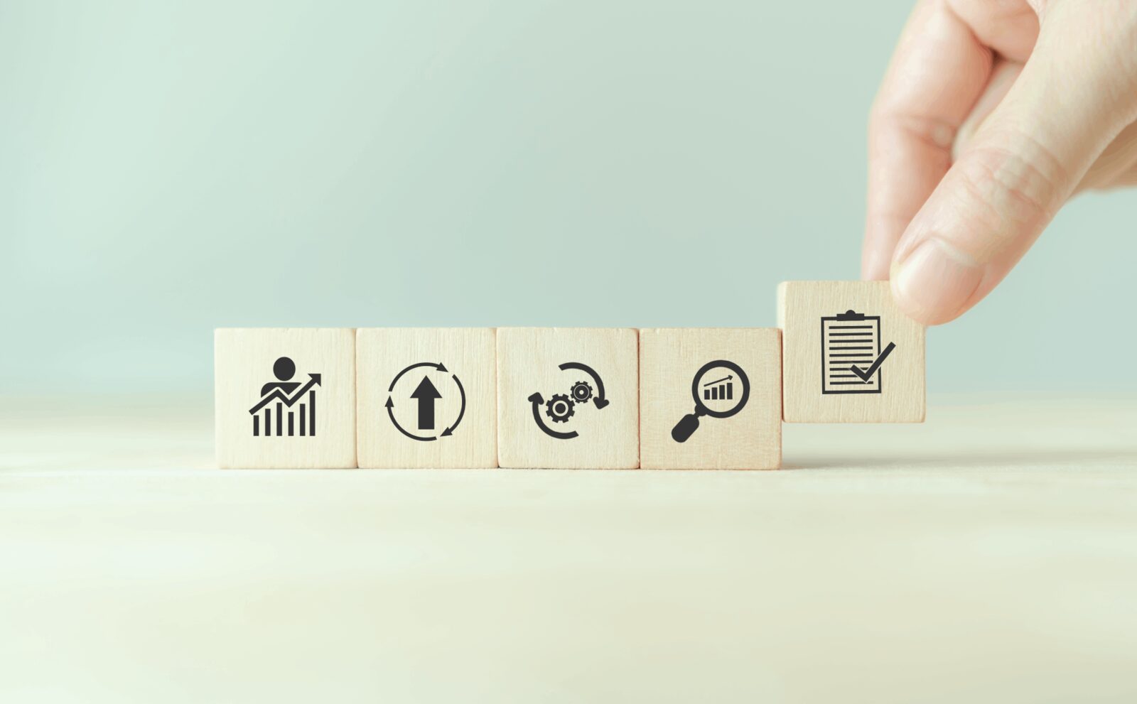 Hand placing the final block in a row of icons ending with a checklist