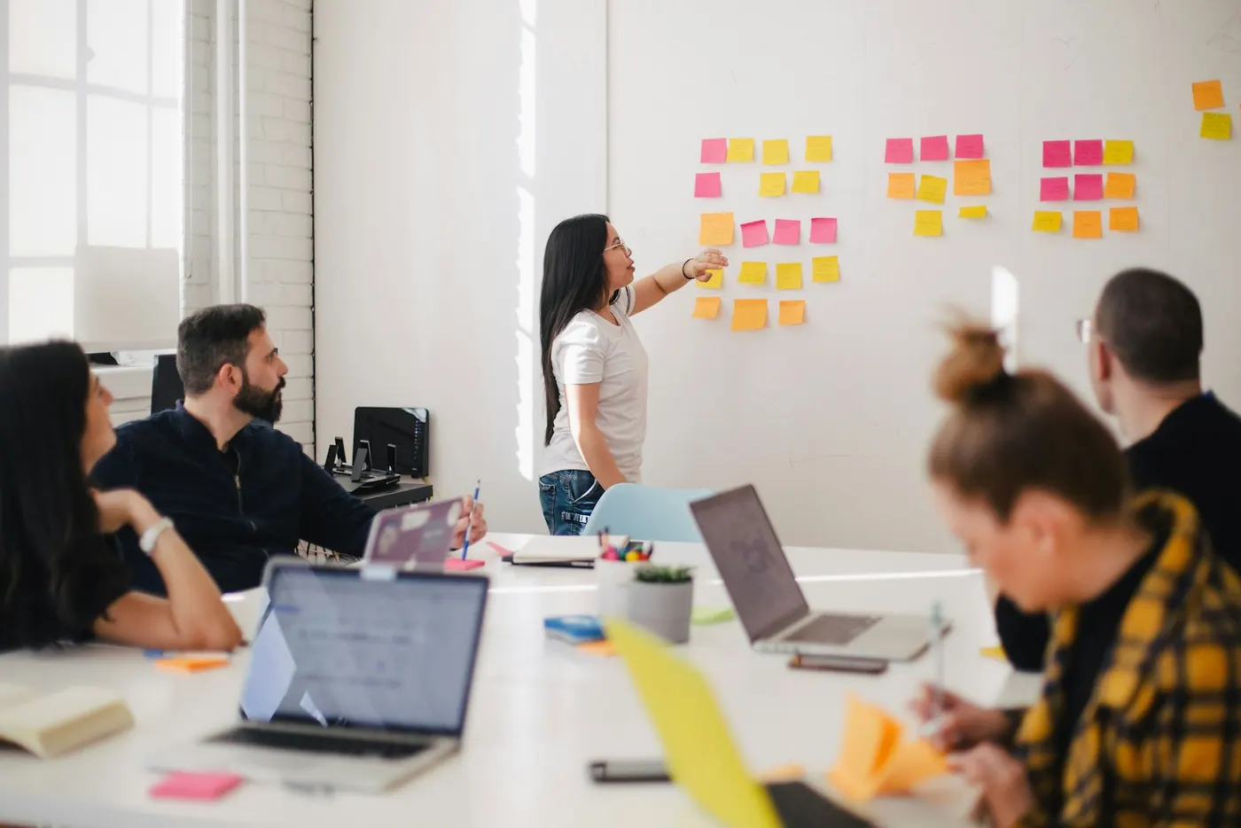 A woman presents ideas on sticky notes during a team meeting, demonstrating collaborative problem solving for vocational.