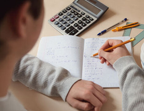 A person studies with a calculator, notebook and writing utensils on a desk for vet compliance.