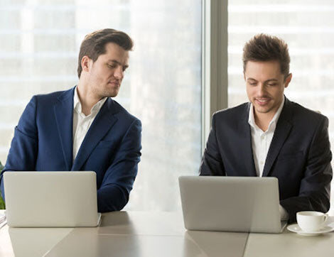 Two businessmen work on laptops, discussing training resources and vet compliance.